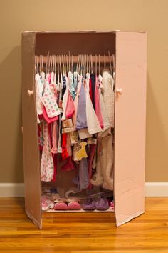 an open cardboard box with clothes hanging in it on a wooden floor next to a wall