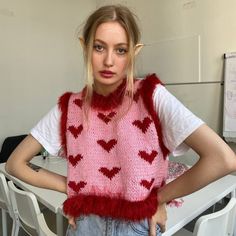 a woman standing in front of a table wearing a pink sweater with hearts on it