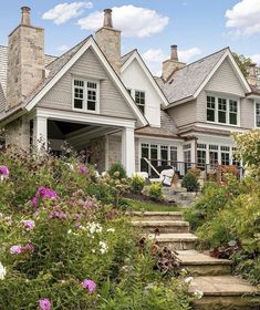 a house with steps leading up to it and flowers in the foreground, on a sunny day