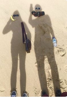 two people standing in the sand with their shadows on them and one person wearing sunglasses