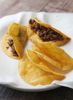 some tacos are on a white plate with paper napkins and wood table in the background