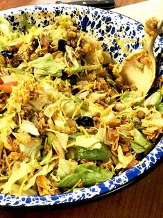 a blue and white bowl filled with salad on top of a wooden table next to utensils