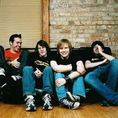 four young men sitting on a couch in front of a brick wall and wooden floor