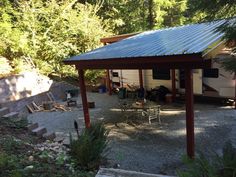 a small house with a metal roof in the middle of some trees and gravel area