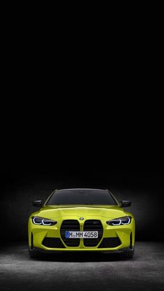 the front end of a yellow bmw sports car in a dark room with its lights on