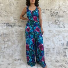 Vintage flowy wide leg jumpsuit Blue and purple tropical leaf print Brand: All that Jazz Fits size M/L -Shoulders: 11" -Bust: 19" -Waist: 17" -Hips: 26" -Length: 55.5" In excellent vintage condition *Model is 5'2"/Bust 33"/Waist 26"/Typically wears XS/S* **Pinned back to show true form Spring Blue Tropical Print Jumpsuits And Rompers, Casual Purple Floral Print Jumpsuits And Rompers, Purple Sleeveless Jumpsuit For Vacation, Blue Tropical Print Jumpsuits And Rompers For Beach, Fitted Floral Print Tropical Jumpsuit, Tropical Floral Print Sleeveless Jumpsuit, Tropical Sleeveless Floral Jumpsuits And Rompers, Sleeveless Tropical Print Jumpsuits And Rompers, Purple Tropical