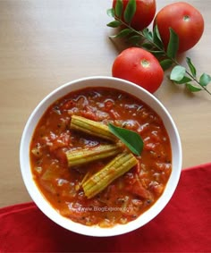 a white bowl filled with tomato soup next to some tomatoes and green garnish