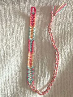 a pink, yellow and blue bracelet laying on top of a white blanket next to a pair of scissors