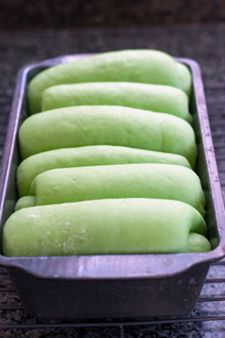 six green doughnuts in a metal pan on a cooling rack, ready to go into the oven