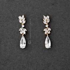 two pairs of gold tone earrings with crystal stones and leaves on them, sitting on a gray surface