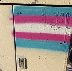 graffiti on the side of a building with pink, blue and white stripes painted on it