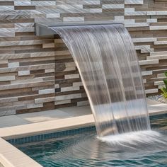 a water fountain in the middle of a pool surrounded by stone wall panels and plants