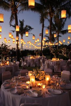 an outdoor dinner setting with paper lanterns hanging from the ceiling and candles lit up in the air