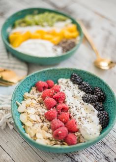 two bowls filled with granola, berries and yogurt on top of a table