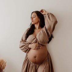 a pregnant woman in a brown dress poses for the camera with her hands on her head