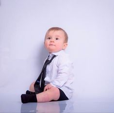 a little boy sitting on the floor wearing a tie and dress shirt with his legs crossed