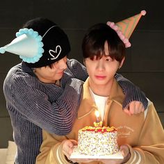 two people are holding a cake with candles on it and one is wearing a party hat