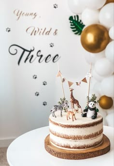 there is a cake with animals on it and balloons in the backgroung wild & three