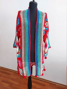 a colorful crocheted cardigan on a mannequin head stand in front of a white wall