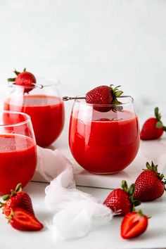 three glasses filled with red liquid and some strawberries on the table next to them