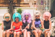 four women dressed in wigs and sunglasses sitting on a bench with drinks at their feet