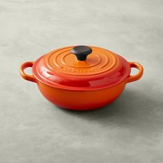 an orange cast iron casserole with black knob on the lid sits on a concrete surface