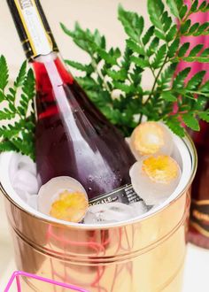 two bottles of wine and some ice in a metal bucket on a table with plants