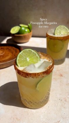 two glasses filled with drinks sitting on top of a table next to some limes