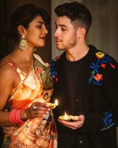 a man and woman standing next to each other while holding candles in their hands as they look at each other