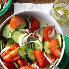 a white bowl filled with cucumbers, tomatoes and other veggies on top of a wooden table