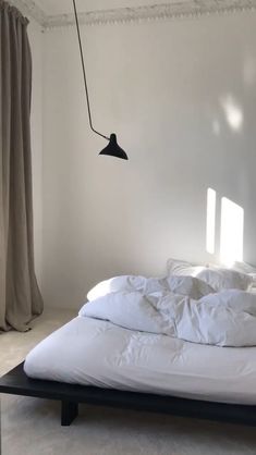 an unmade bed with white sheets and pillows in a room that has light coming through the windows