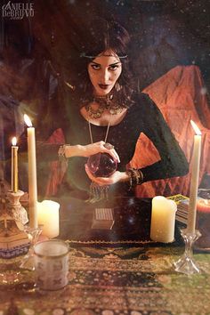 a woman holding a crystal ball in front of candles and other items on a table