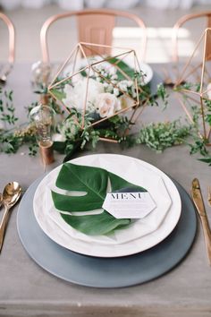 a table set with plates, silverware and greenery