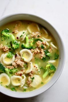 a white bowl filled with pasta and broccoli soup on top of a table