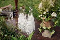 three glass bottles sitting on top of a wooden table next to flowers and greenery