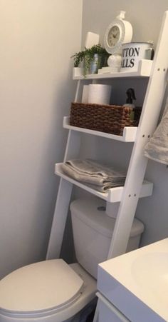 a white toilet sitting next to a bathroom sink under a ladder shelf filled with towels