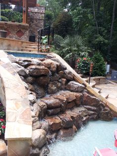 an outdoor swimming pool with rocks and water running down it's sides, surrounded by landscaping