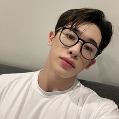 a young man with glasses is sitting on a couch looking at the camera while wearing a white t - shirt