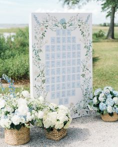 flowers in baskets are sitting next to a wedding seating chart on a table with blue and white flowers