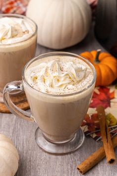 two mugs of hot chocolate with whipped cream on top and pumpkins in the background