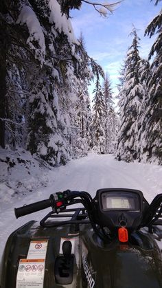 an atv driving down a snow covered road in the middle of winter with trees on both sides