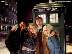 four people posing in front of a police box at night with the doctor who is standing next to them