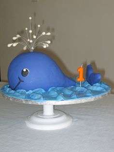 a cake shaped like a blue whale on top of a white tablecloth with an orange candle sticking out of it's mouth