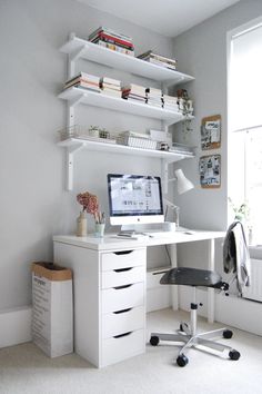 a desk with a computer on top of it next to a window and bookshelves