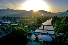 an aerial view of a bridge over a river at sunset with mountains in the background