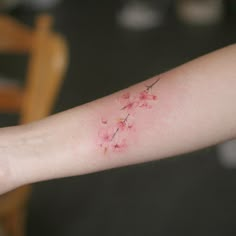 a woman's arm with pink flowers on it and a small bird flying over the branch