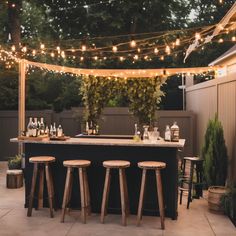 an outdoor bar with stools and lights strung across the top, surrounded by greenery