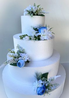 three tiered white cake with blue flowers and greenery