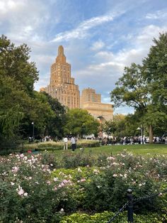 people are walking around in the park with flowers and trees on either side of them