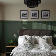 a bedroom with green paneling and white bedding, two framed pictures on the wall